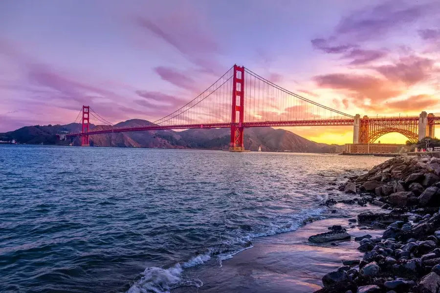 El puente Golden Gate al atardecer con un cielo multicolor y la Bahía de San Francisco en primer plano.